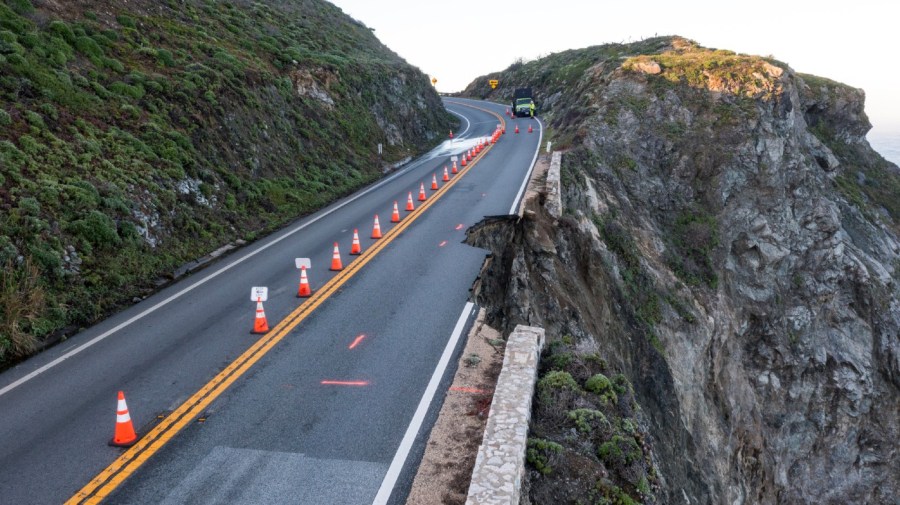 Cones mark a break in a lane along a cliff face.