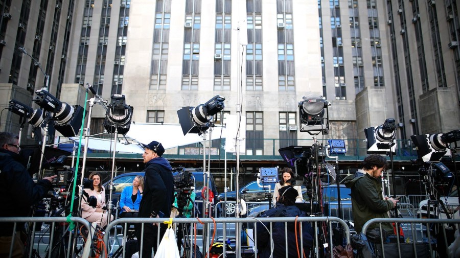 Members of the media are lined up with camera equipment outside a courthouse.