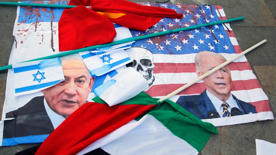 Printouts scattered on the ground show U.S. and Israeli flags splattered in red paint with the faces of President Biden and Prime Minister Benjamin Netanyahu.