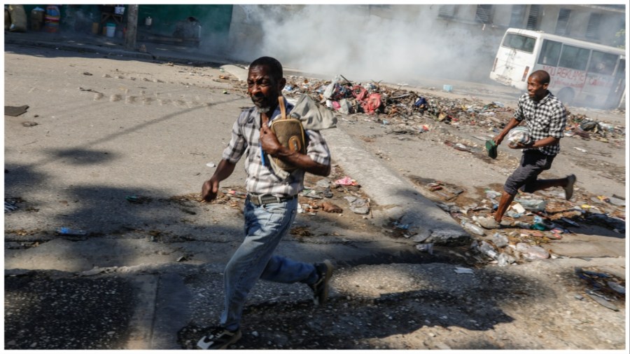 Men run for cover as riot police launch tear gas in an effort to disperse people near the National Palace, in Port-au-Prince, Haiti, Tuesday, April 2, 2024. (AP Photo/Odelyn Joseph)