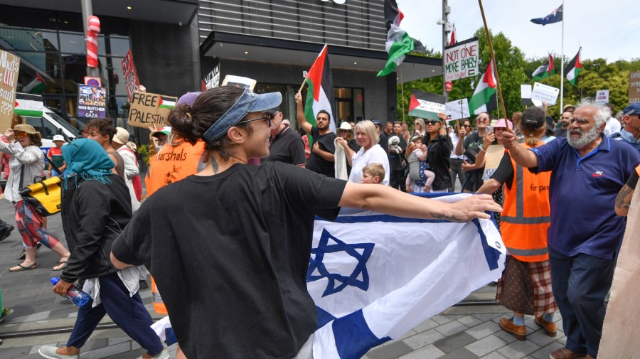 A pro-Israeli supporter is waving the flag of Israel as pro-Palestinian supporters march past them during a march in Christchurch, New Zealand, on December 9, 2023.