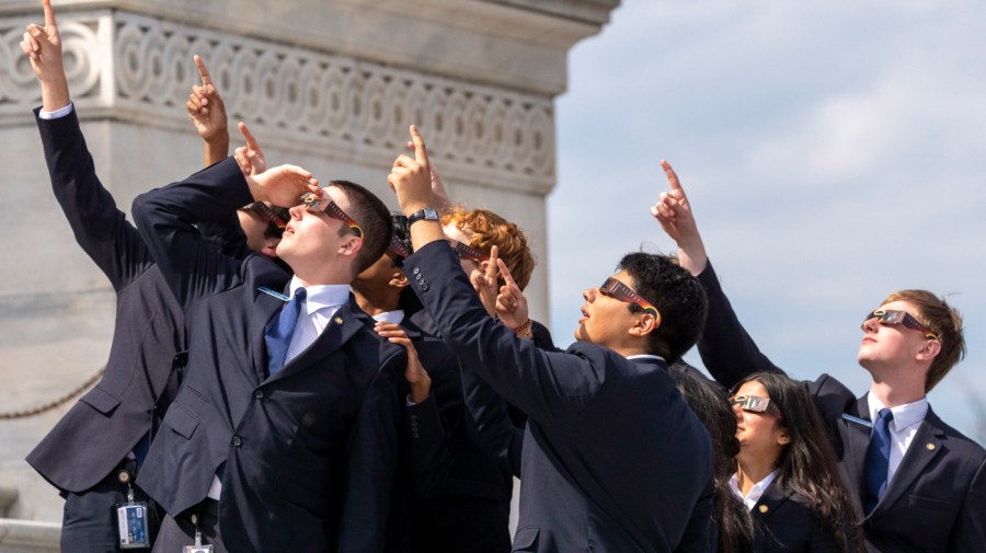 Senate pages wear eclipse glasses as they view the moon partially covering the sun during a total solar eclipse, in front of the U.S. Senate on Capitol Hill, Monday, April 8, 2024, in Washington.