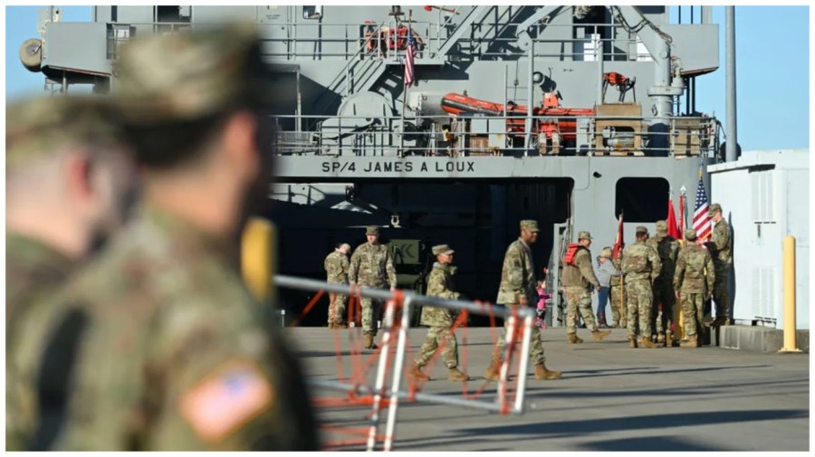 Crew members walk past a vessel as others prepare it to set sail.