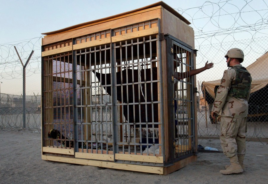 FILE - A detainee in an outdoor solitary confinement cell talks with a military police officer at the Abu Ghraib Prison on the outskirts of Baghdad, Iraq, June 22, 2004. A judge declared a mistrial Thursday, May 2, 2024, after a jury said it was deadlocked and could not reach a verdict in the trial of a military contractor accused of contributing to the abuse of detainees at the Abu Ghraib Prison in Iraq two decades ago. (AP Photo/John Moore, File)