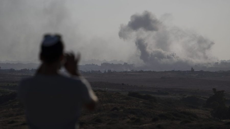 A man watches smoke rising to the sky in the distance.