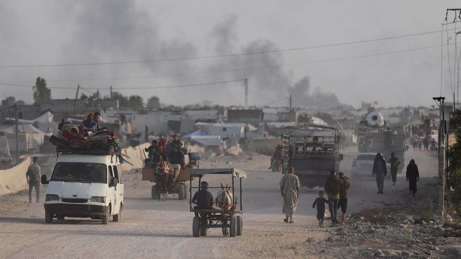 Palestinians in cars and horse-drawn carts are seen in a road.