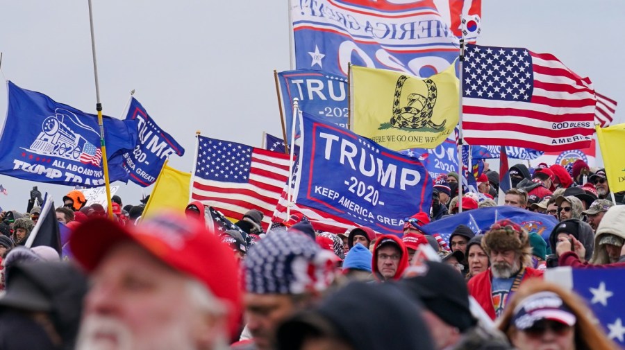 American flags and flags supporting former President Trump are flown in a crowd of people.