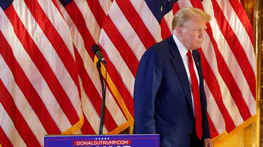 Former President Trump walks in front of a backdrop of American flags.