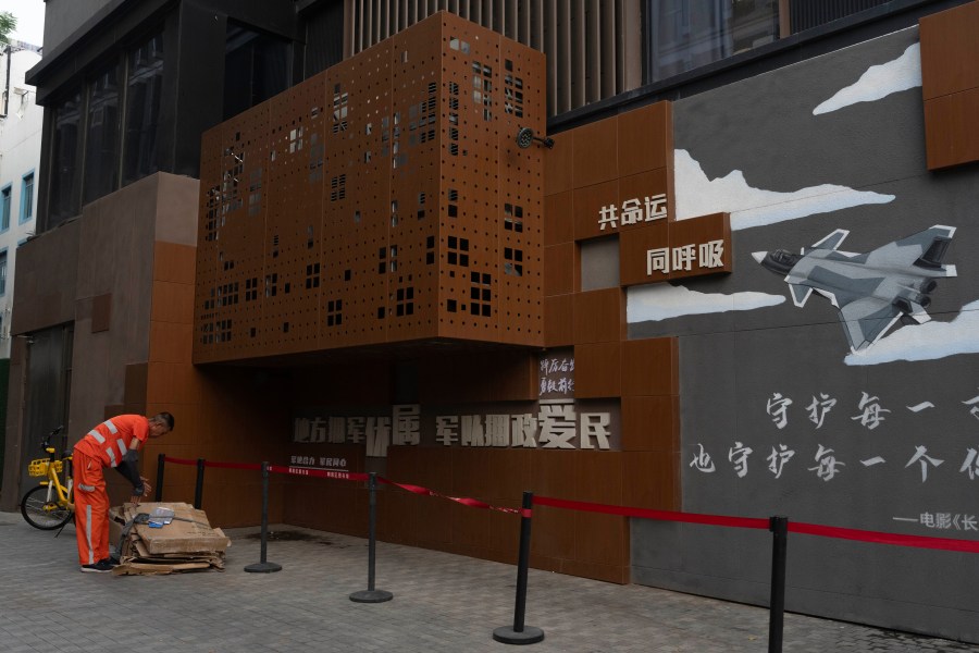 A municipal worker collects scrap cardboard near a mural calling for Military and Civilian Unity in Beijing, Thursday, June 13, 2024. Chinese state media say that a military history buff found a collection of confidential documents related to the country's military in a pile of old papers he bought for under $1. (AP Photo/Ng Han Guan)