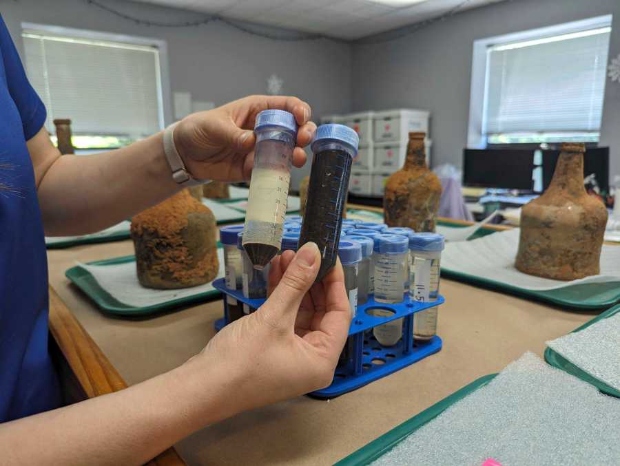 Curator Lily Carhart holds up different samples of liquid they extracted from a few dozen 18th-century glass bottles that contained fruit after they were unearthed from the cellar of George Washington's residence in Mount Vernon, Va., Monday, June 17, 2024. (AP Photo/Nathan Ellgren)