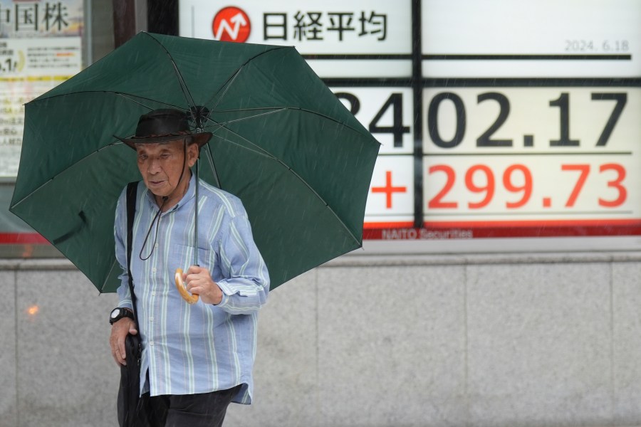 A person walks in the rain in front of an electronic stock board showing Japan's Nikkei 225 index at a securities firm Tuesday, June 18, 2024, in Tokyo. Shares were mostly higher in Asia on Tuesday after U.S. stocks rallied to more records, with gains for technology companies pushing the benchmarks higher. (AP Photo/Eugene Hoshiko)