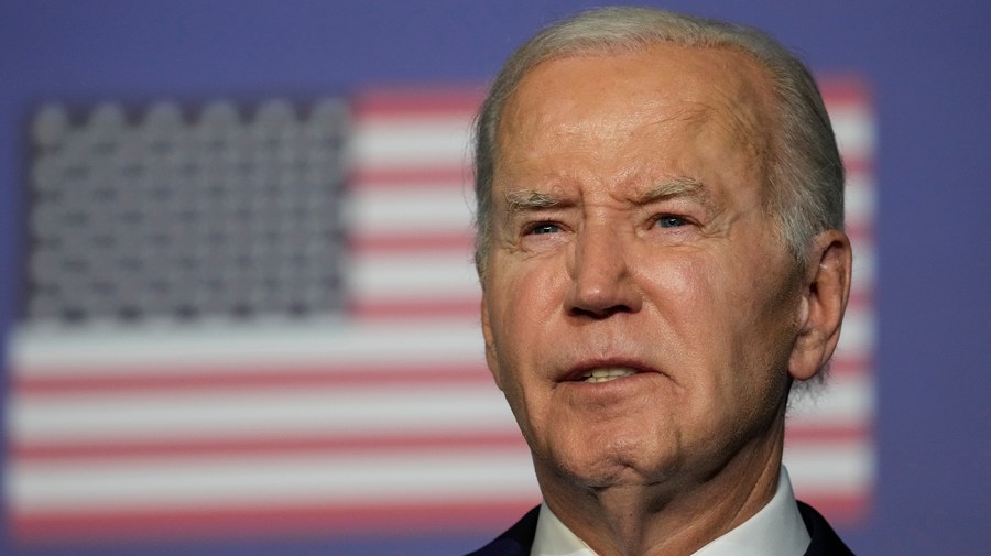 President Biden is seen in a close-up in front of an American flag.