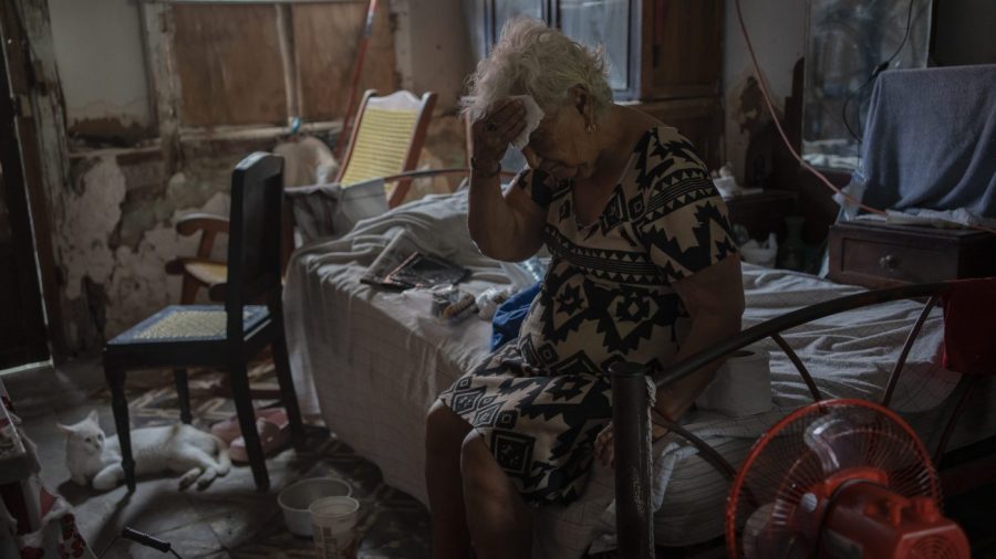 A woman wipes sweat from her forehead with a tissue while sitting on a bed.