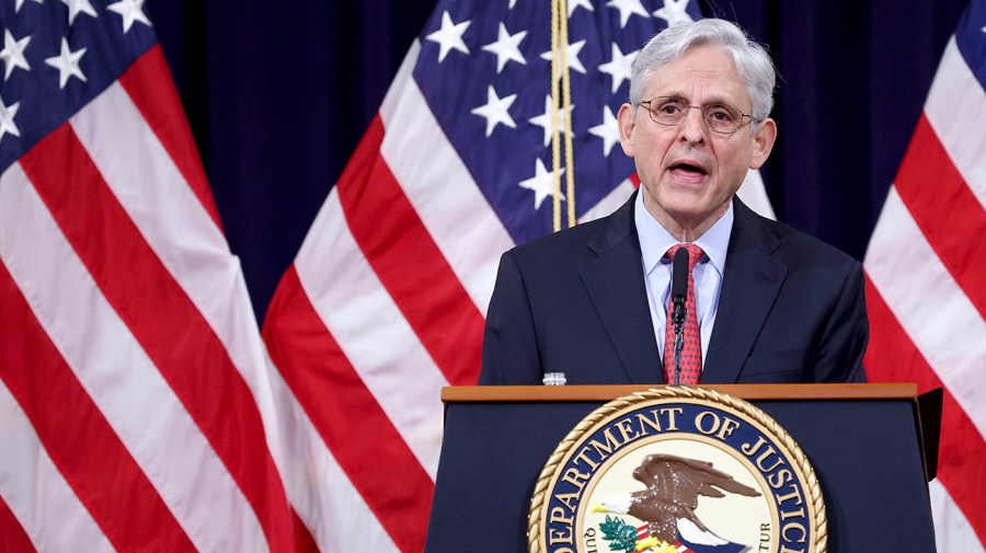 Attorney General Merrick Garland speaks at a podium in front of several American flags.