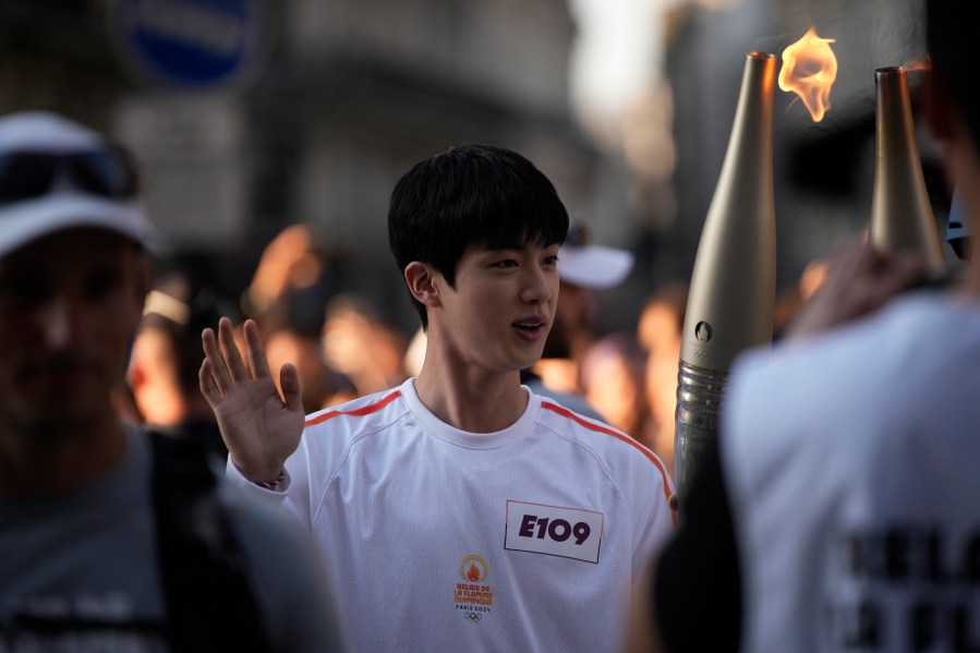 Jin, the oldest member of K-pop supergroup BTS, takes the Olympic torch, Sunday, July 14, 2024 in Paris. Jin will carry the Olympic torch in the area of Paris' Louvre Museum after recently completing his mandatory military service. (AP Photo/Louise Delmotte)