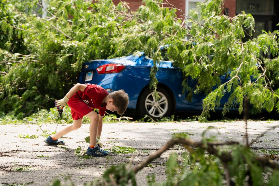 Ezra Solomon, 8, helps clear the road of debris near the intersection of West Huron and North Leavitt streets in Chicago's West Town neighborhood, Tuesday, July 16, 2024, after severe storms passed through the Chicago area the night before. (Pat Nabong/Chicago Sun-Times via AP)