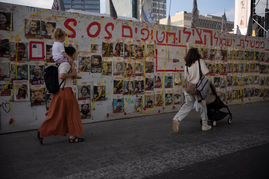 People walk past a wall with photos of hostages held in the Gaza Strip at a plaza known as Hostages Square in Tel Aviv, Israel Tuesday, July 16, 2024. (AP Photo/Leo Correa)