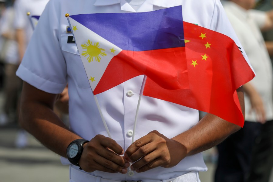 FILE - A member of the Philippine Coast Guard holds flags during the arrival of Chinese naval training ship, Qi Jiguang, for a goodwill visit at Manila's port, Philippines, June 14, 2023. (AP Photo/Basilio Sepe, File)