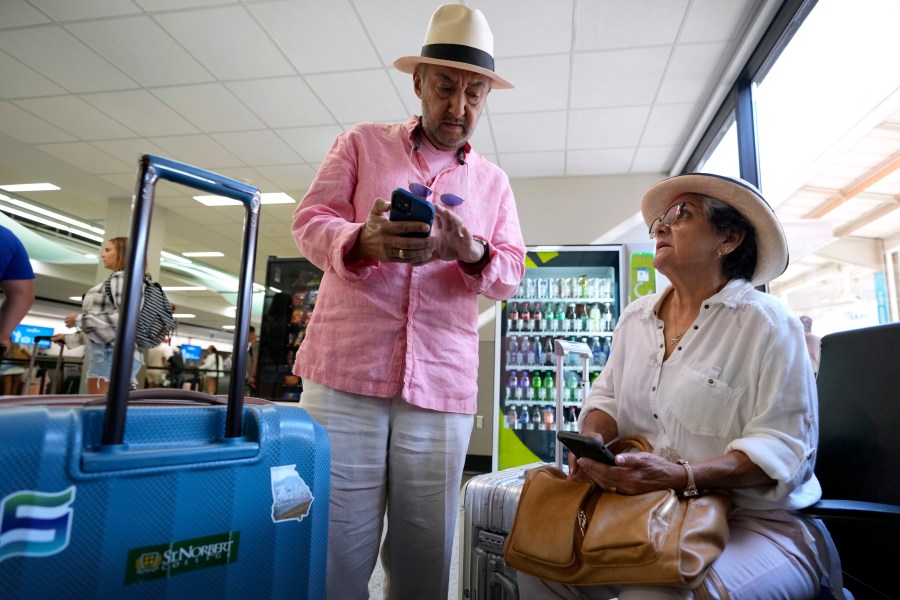 Jose Angel Saavedra, left, and his wife Sara, of Johnston, Iowa, look at their cell phones while trying to book a flight after their original flight was cancelled, Friday, July 19, 2024, at the Des Moines International Airport in Des Moines, Iowa. (AP Photo/Charlie Neibergall)