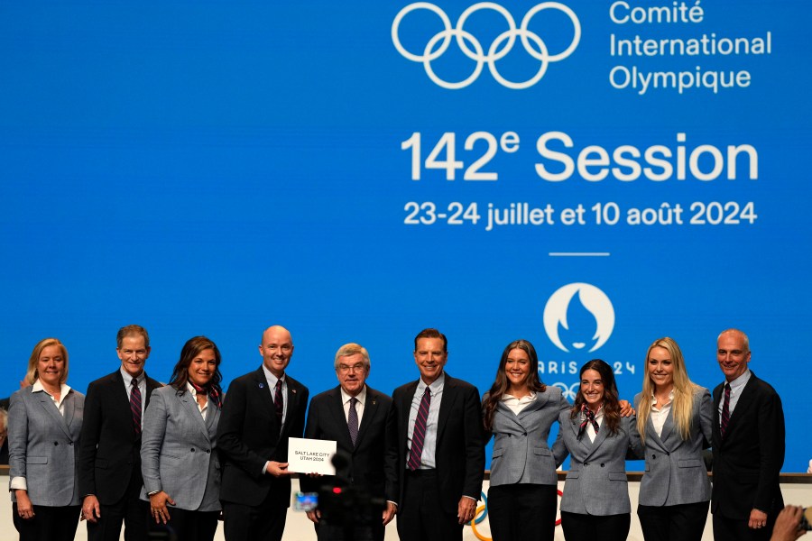 Utah Gov. Spencer Cox, fourth left, and IOC president Thomas Bach, center, pose with the Salt Lake City delegation during the 142nd IOC session at the 2024 Summer Olympics, Wednesday, July 24, 2024, in Paris, France, after Salt Lake City was confirmed as host for the 2034 Winter Games by International Olympic Committee. (AP Photo/Natacha Pisarenko)