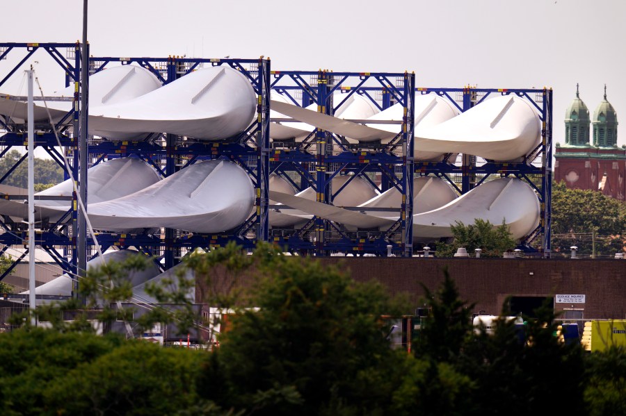 FILE - Giant wind turbine blades for the Vineyard Winds project are stacked on racks in the harbor, July 11, 2023, in New Bedford, Mass. The maker of a massive wind turbine blade that broke apart off Nantucket Island and washed up on the beaches says a manufacturing problem was responsible. (AP Photo/Charles Krupa, File)