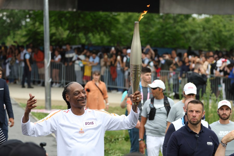 Snoop Dogg carries the Olympic torch at the 2024 Summer Olympics, Friday, July 26, 2024, in Saint-Denis, outside Paris, France. (AP Photo/Aurelien Morissard)