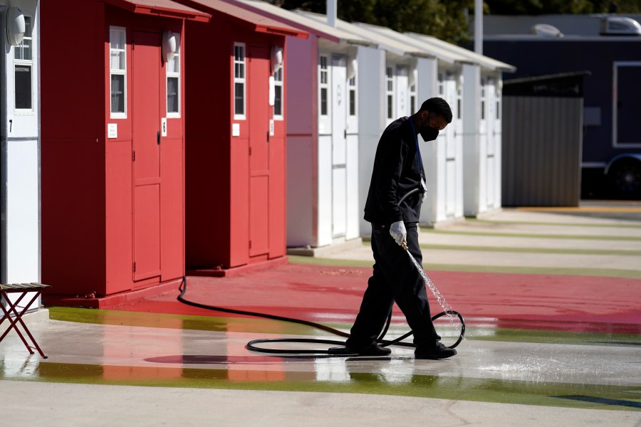 FILE - A worker cleans in front of a row of tiny homes for homeless people in the North Hollywood section of Los Angeles on Feb. 25, 2021. (AP Photo/Marcio Jose Sanchez, File)