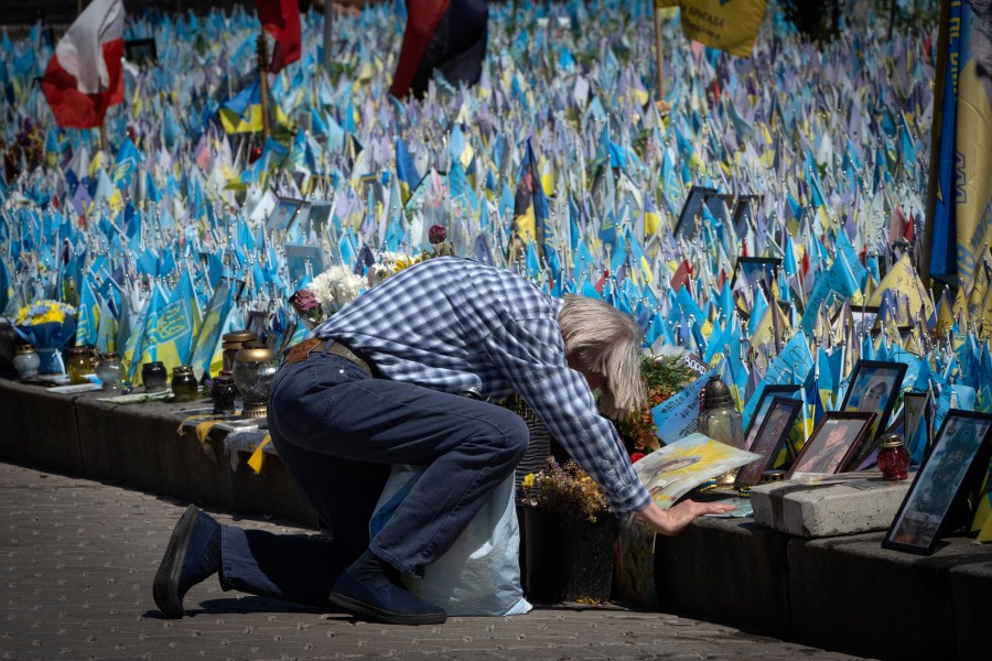 A man kneels in front of a makeshift memorial for fallen Ukrainian soldiers on Independence Square in Kyiv, Ukraine, Tuesday, July 23, 2024. Each flag brought by relatives bears a name of a soldier killed in battle with Russian troops. (AP Photo/Efrem Lukatsky)