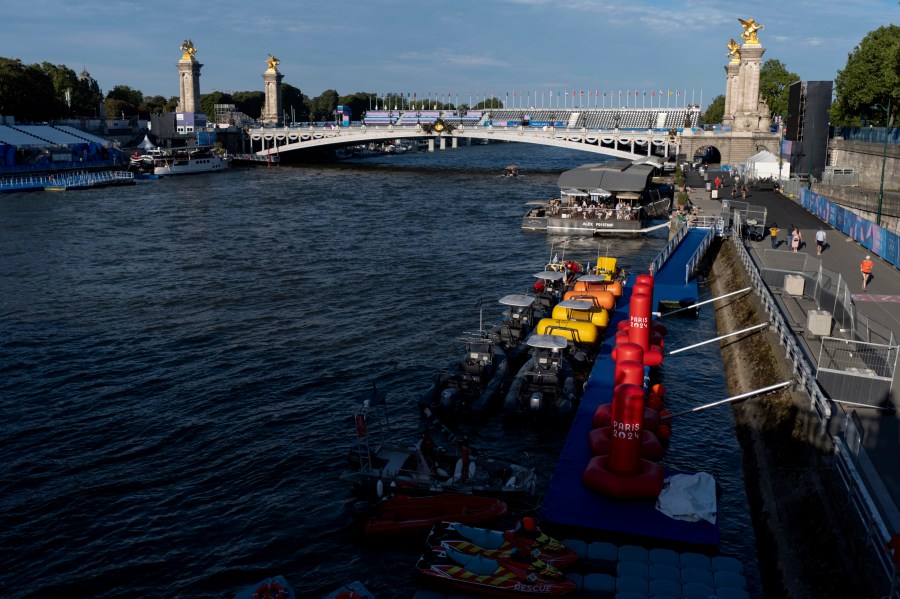 Watercraft and buoys sit along the Seine river as the triathlon event venue on the Pont Alexandre III bridge stands in the background at the 2024 Summer Olympics, Sunday, July 28, 2024, in Paris. (AP Photo/David Goldman)