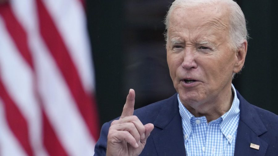 President Biden points his finger while speaking in front of an American flag.