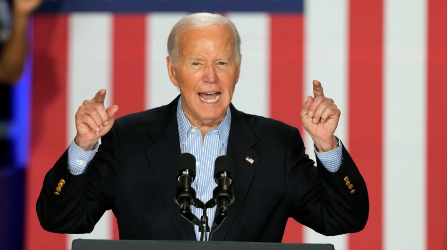 President Biden dramatically points his fingers while in front of large red-and-white stripes at an event.