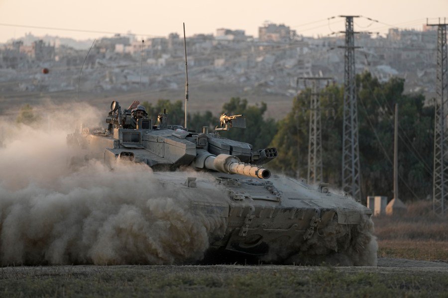 With destroyed buildings in the Gaza Strip behind him, an Israeli soldier waves from a tank, near the Israel-Gaza border in southern Israel, Thursday, Aug. 1, 2024. (AP Photo/Tsafrir Abayov)