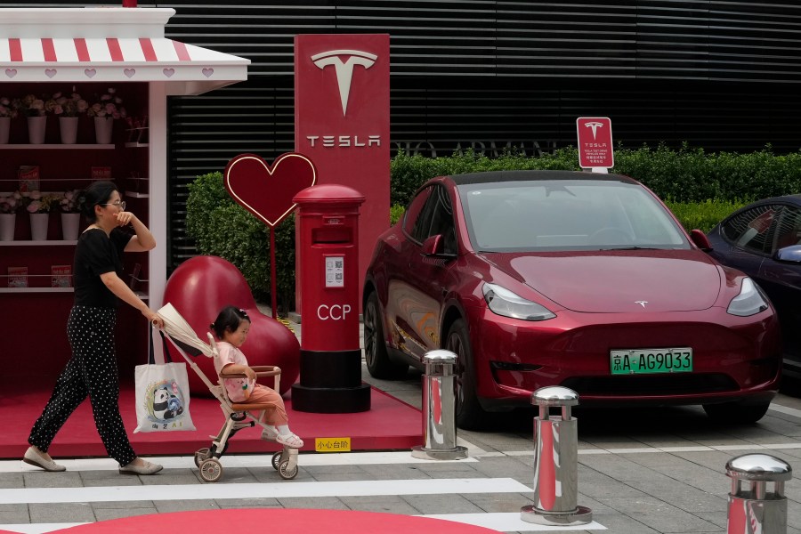 A woman pushes a child past a Red Tesla vehicle at a charging station in Beijing, July 24, 2024. (AP Photo/Ng Han Guan)