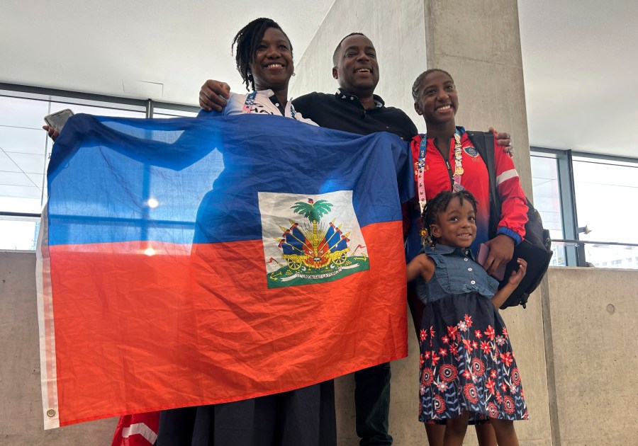 Fourteen-year-old swimmer Mayah Chouloute and her family pose for a photo with the Haitian flag after her first Olympic race, Aug. 1, 2024, in Paris, France. (AP Photo/Megan Janetsky)