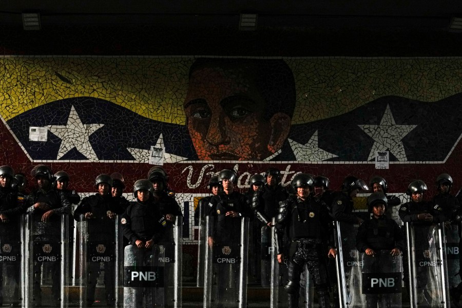 Bolivarian National Police stand guard in front of a mural with an image of independence hero Simon Bolivar in Caracas, Venezuela, Wednesday, July 31, 2024. (AP Photo/Matias Delacroix)