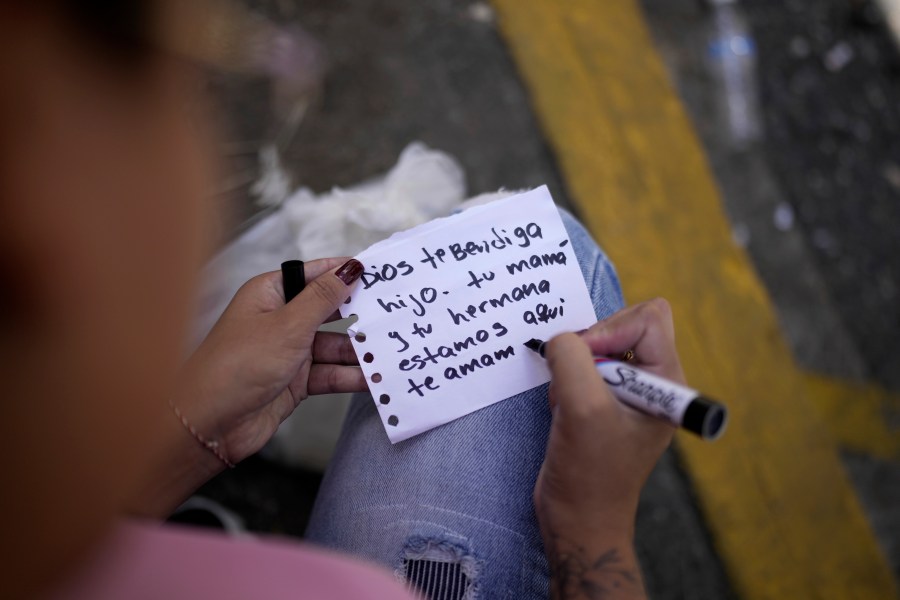 FILE - Franchesca Aponte writes a note to her brother outside the Boleita National Police detention center after he was arrested during the recent protests against President Nicolas Maduro's reelection, in Caracas, Venezuela, Thursday, Aug. 1, 2024. The note from Aponte and her mother reads in Spanish: "God bless you son. Your mother and sister are here. We love you." (AP Photo/Matias Delacroix, File)