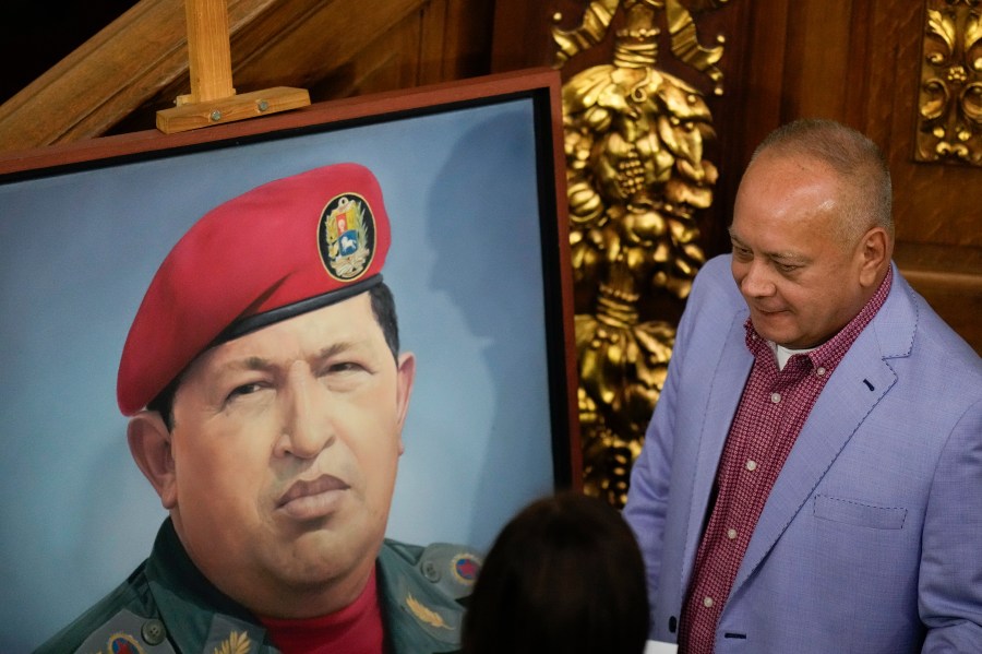 Lawmaker Diosdado Cabello stands next to an image of late President Hugo Chavez in Congress as the National Assembly debates a bill that controls and regulates NGOs, in Caracas, Venezuela, Tuesday, Aug. 13, 2024. (AP Photo/Matias Delacroix)