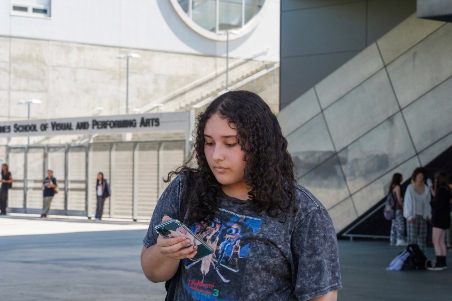 Student April Yamilet, 17, uses her cellphone as she steps outside the Ramon C. Cortines School of Visual and Performing Arts High School in downtown Los Angeles on Tuesday, Aug. 13, 2024. (AP Photo/Damian Dovarganes)