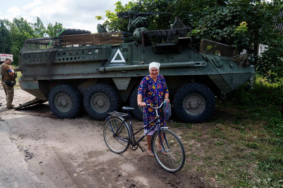 A local woman hauls her bicycle in front of Ukrainian APC near Russian-Ukrainian border, Sumy region, Ukraine, Wednesday, Aug. 14, 2024. (AP Photo/Evgeniy Maloletka)