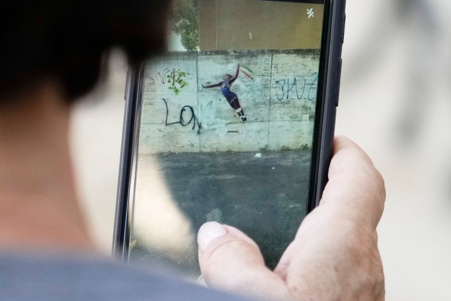 A woman takes a picture at Laika's street-art celebration of Paola Egonu, who helped lead Italy to its first-ever Olympic gold medal in women's volleyball, in Rome, Wednesday, Aug. 14, 2024. A day after images of the graffiti began circulating, someone painted over Laika's original work, turning Egonu's dark skin pink and blurring out the words on the volleyball. At some point on Tuesday, someone used a dark marker to try to restore Laika's original design. (AP Photo/Gregorio Borgia)