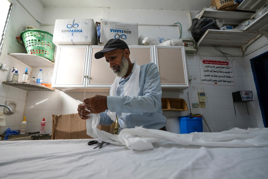 Palestinian morgue worker Nawaf al-Zuriei, a morgue worker prepares a burial shroud at at Deir al-Balah's Al-Aqsa Martyrs Hospital in the Gaza Strip, Friday, Aug. 4, 2024. Those killed by the war are considered ritually pure under Islamic tradition, so their bodies are not washed, he said. Workers cover the damaged bodies in plastic to avoid bloodstains on white shrouds. (AP Photo/Abdel Kareem Hana)