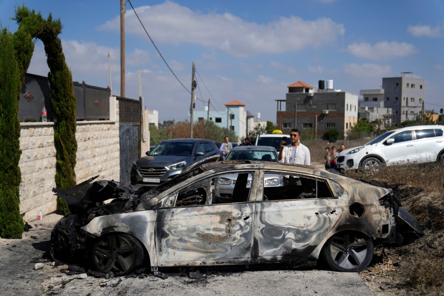 A Palestinian films a torched vehicle, seen the morning after a rampage by Israeli settlers in the West Bank village of Jit, Friday, Aug. 16, 2024. (AP Photo/Nasser Nasser)