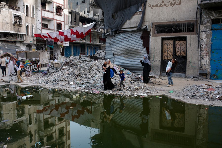 FILE - Palestinians displaced by the Israeli air and ground offensive on the Gaza Strip walk next a dark streak of sewage flowing into the streets of the southern town of Khan Younis, Gaza Strip, Thursday, July 4, 2024. Health authorities and aid agencies are racing to avert an outbreak of polio in the Gaza Strip after the virus was detected in the territory's wastewater and three cases with a suspected polio symptom have been reported. (AP Photo/Jehad Alshrafi, File)