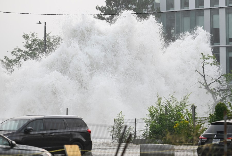 A broken water main spews water into the air on a street in Montreal, Friday, Aug. 16, 2024, causing flooding in several streets of the area. (Graham Hughes/The Canadian Press via AP)