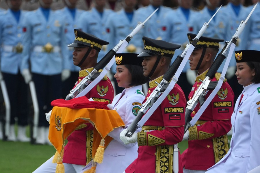 A bearer is escorted by members of a honor guard as she carries the national Red-White flag to be hoisted during the ceremony marking Indonesia's 79th anniversary of independence at the new presidential palace in its future capital of Nusantara, a city still under construction on the island of Borneo, Saturday, Aug. 17, 2024. (AP Photo/Achmad Ibrahim)