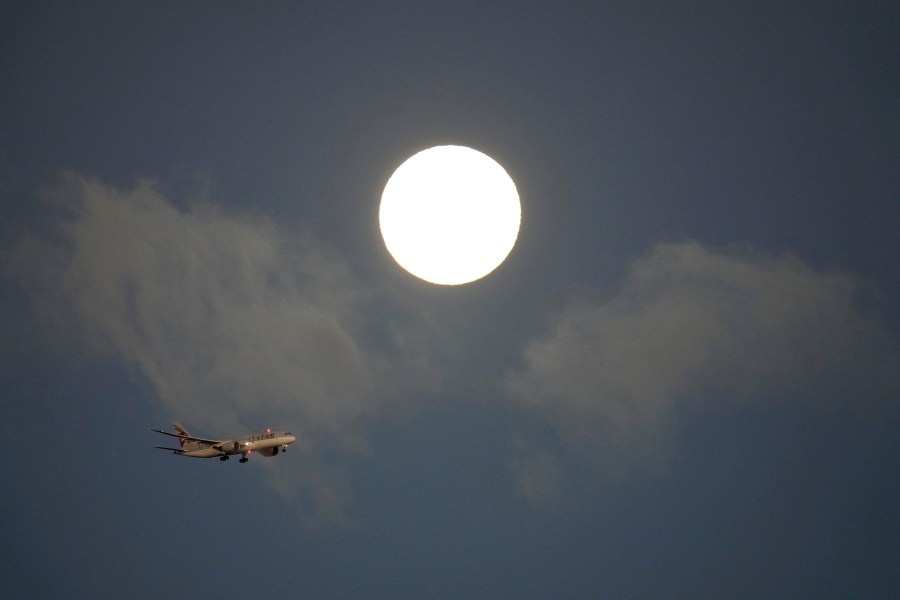 A Qatar Airways jetliner approaches for landing in Lisbon, with a supermoon in the background, at sunrise Tuesday, Aug. 20, 2024. (AP Photo/Armando Franca)