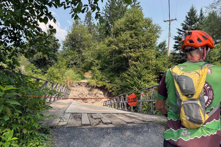 A cyclist looks at a closed flood-damaged bridge at Kingdom Trails in Burke, Vt., Aug. 14, 2024. (AP Photo/Lisa Rathke)