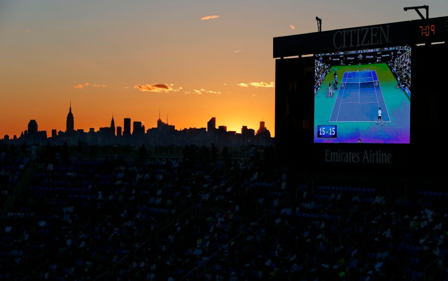 FILE - The championship match between Britain's Andy Murray and Serbia's Novak Djokovic is shown on a big screen as the sun sets behind the New York City skyline at the 2012 U.S. Open tennis tournament, Monday, Sept. 10, 2012, in New York. The 2024 U.S. Open begins Monday, Aug. 26.(AP Photo/Julio Cortez, File)