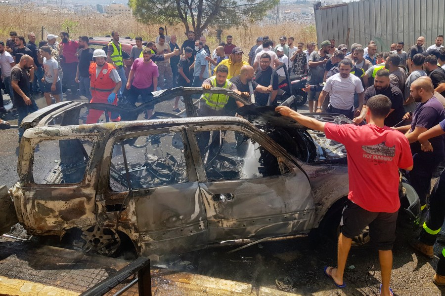 Civil Defense workers and citizens inspect the remains of a burned car that was hit by an Israeli strike in the southern port city of Sidon, Lebanon, Monday, Aug. 26, 2024. (AP Photo/Mohammed Zaatari)