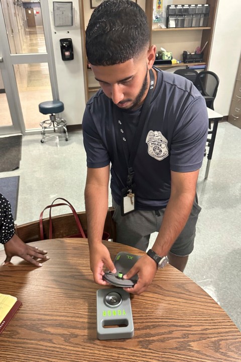 Lackawanna Police Officer Abdul Albaneh, who works with schools, demonstrates how to unlock a cellphone pouch that will prevent students from using their cellphones during the school day to improve student engagement, in Lackawanna, N.Y., Aug. 19, 2024, for when school resumes in September. (AP Photo/Carolyn Thompson)